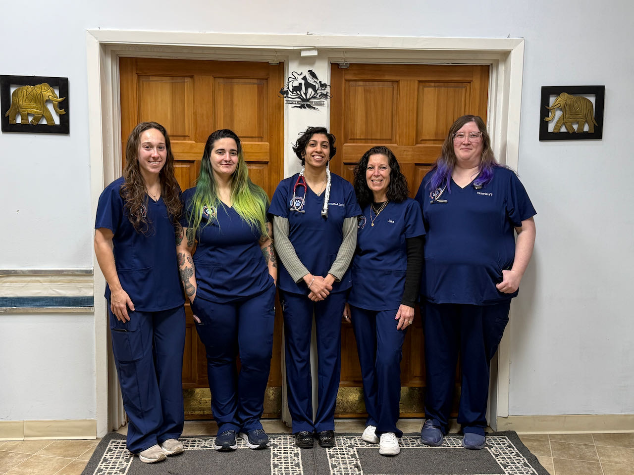 Team picture in lobby.  5 team members are in matching dark blue scrubs with the vet in the center.