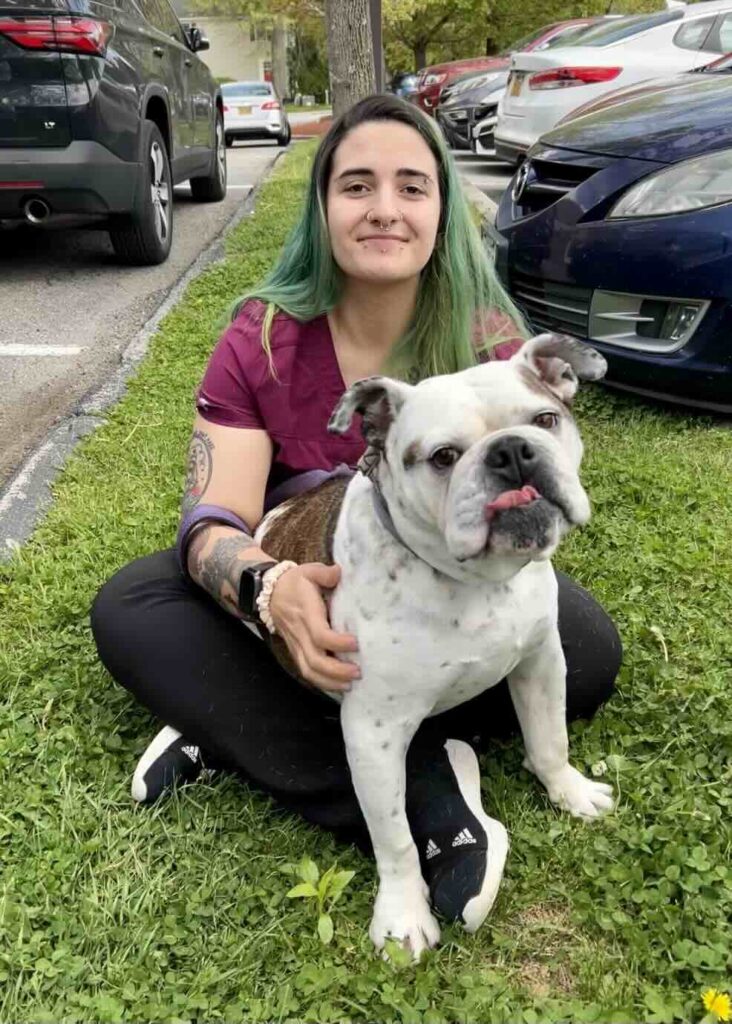 Veterinary assistant with green hair sitting outdoors with white and brown bulldog